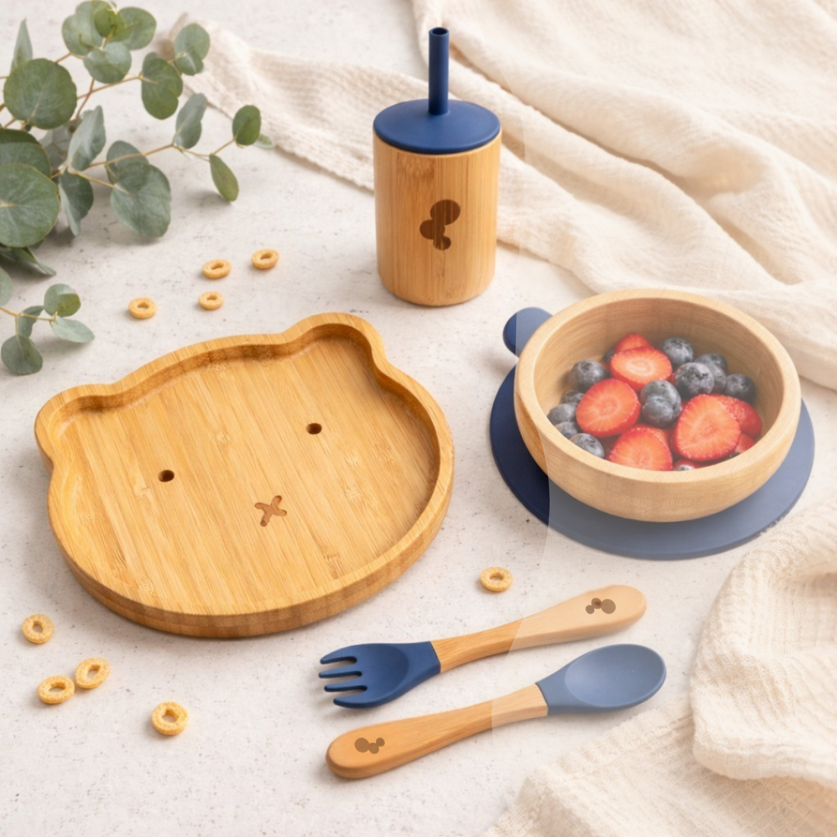 Baby and toddlers bamboo tableware weaning set with a bowl, plate, and utensils on a light fabric background.