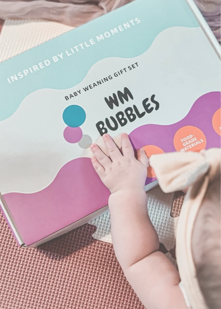 Baby's hand holding a weaning gift set from WM Bubbles